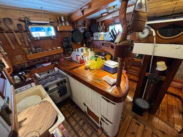 Cette cuisine confortable et compacte est dotée d'armoires en bois, d'une décoration d'inspiration marine, de petits appareils électroménagers, d'ustensiles suspendus et d'un hublot, le tout niché dans l'intérieur charmant et fonctionnel d'un bateau.