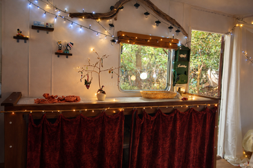 Esta acogedora habitación cuenta con luces de hadas, cortinas de terciopelo rojo, un pequeño árbol decorado, figuritas caprichosas, una gran ventana y detalles de madera natural, que crean un ambiente cálido.