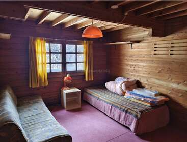 Esta acogedora habitación, decorada al estilo de una cabaña de madera, cuenta con una cama individual, un sofá, cortinas amarillas, una mesita de noche con lámpara y un ambiente cálido y acogedor.
