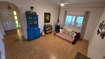 Ce salon confortable se caractérise par une armoire bleue, des sièges bas avec de nombreux coussins, des jouets, un sol en bois, une grande fenêtre, des murs clairs et diverses décorations murales, créant ainsi de la chaleur.