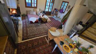 Un salon chaleureux avec des tapis, une cheminée, une table à manger dressée pour le petit-déjeuner, une chaise haute et un enfant qui joue près d'un canapé orné de coussins.