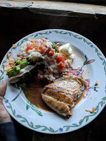 Assiette de poisson grillé avec sauce, riz garni de tomates, brocolis et beurre, servie sur une assiette en céramique à motif floral. Cadre rustique.