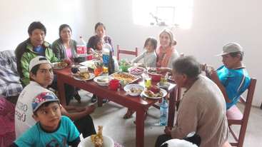 La imagen representa a un grupo de personas reunidas en torno a una mesa, probablemente celebrando una ocasión especial, con un ambiente festivo y un sentimiento de comunidad y unión.