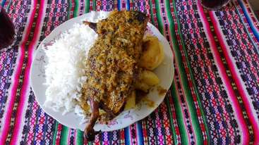 La imagen representa un plato de comida con un gran trozo de carne, acompañado de un cuenco de arroz y un vaso de líquido, sobre un fondo neutro. La escena parece una composición de naturaleza muerta.