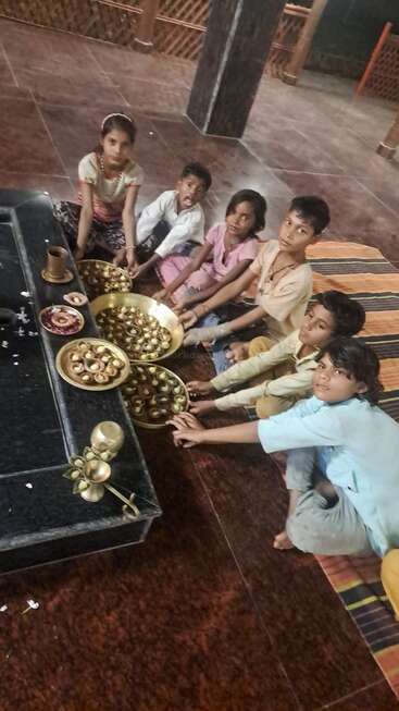 Seis niños están sentados en el suelo, con bandejas de lámparas de aceite tradicionales, posiblemente preparándose para una ceremonia religiosa o cultural en un templo.