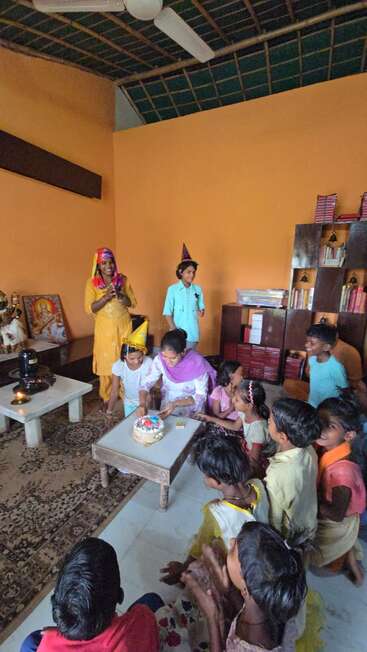 Un grupo de niños y una mujer se reúnen alrededor de una mesa para celebrar un cumpleaños. Hay una tarta, sombreros de fiesta, sonrisas y un ambiente festivo en una acogedora sala.