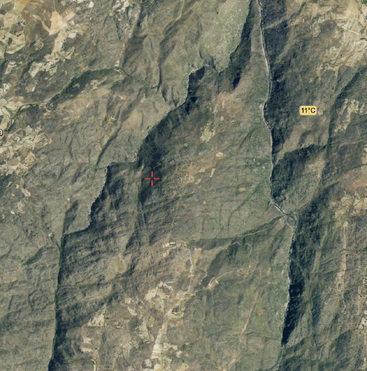 An aerial satellite image shows a mountainous, rugged terrain with sparse vegetation. A red cross marks a central point; a temperature label reads “11°C” on the right.