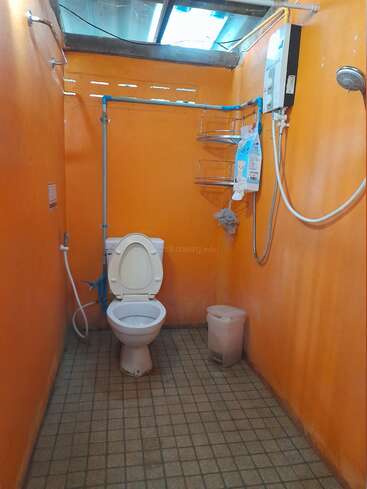 The image depicts a small, orange bathroom with a toilet, shower, and sink, featuring a tiled floor and a skylight above. The walls are painted orange.