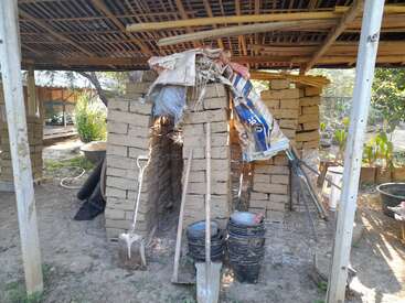The image depicts a rustic outdoor structure, likely a shed or workshop, with a sloping roof and a pile of bricks and tools in the foreground.