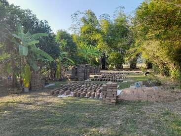 The image depicts a grassy area with trees and a pile of bricks, featuring a stack of bricks in the foreground and a larger pile in the background.