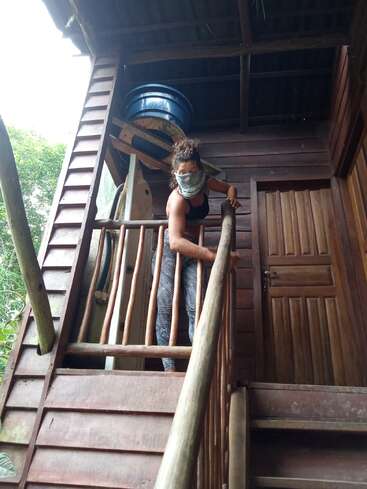 L'image représente une femme debout dans les escaliers d'un bâtiment en bois, portant un masque et arborant un soutien-gorge de sport noir et un legging à motifs.