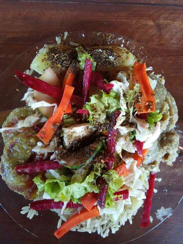 L'image représente une salade vibrante dans une assiette en verre, composée d'un mélange de légumes, de riz et d'autres ingrédients, sur un fond de table en bois foncé.
