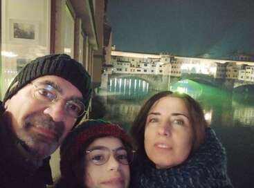 Eine dreiköpfige Familie posiert für ein nächtliches Selfie mit der beleuchteten Brücke Ponte Vecchio und den Spiegelungen über dem Fluss im Hintergrund in Florenz.