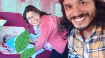 La imagen muestra un selfie borroso de un hombre y una mujer sonriendo, con la mujer con gafas y jersey rosa, sentada en un sofá rojo.