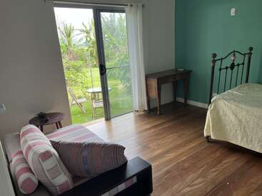 Cette chambre confortable dispose d'un lit en fer ancien, d'un canapé rayé, de sols en bois, d'un bureau et de portes coulissantes en verre qui s'ouvrent sur un patio luxuriant avec des sièges.