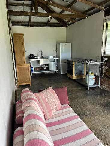 Cette image montre une cuisine rustique avec des chevrons apparents, un canapé rose rayé, un réfrigérateur, un four, un meuble en bois, un évier en acier inoxydable et un sol en béton poli.