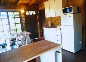This cozy wooden kitchen features a dining table, refrigerator, microwave, white cabinets, and a wooden island, with natural light streaming through large windows and door.