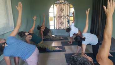 The image depicts a group of individuals engaged in yoga or stretching exercises, with a focus on their bodies and movements, set against a neutral background. The scene conveys a sense of relaxation and mindfulness.