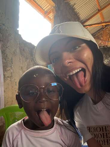 A joyful selfie of a woman and a child, both sticking out their tongues. The child wears large glasses. They seem to be enjoying a playful moment together.
