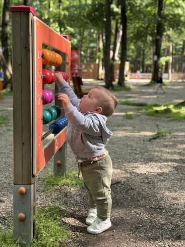 Un jeune enfant en tenue décontractée joue avec un boulier coloré en plein air, entouré d'arbres et de soleil, dans un parc ou un terrain de jeu paisible.
