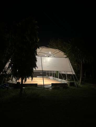 Un pavillon extérieur bien éclairé est vide la nuit, entouré d'arbres et d'herbe. L'obscurité enveloppe la scène, mettant en valeur la structure lumineuse et accueillante qui contraste avec elle.