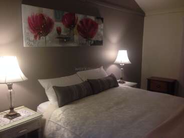 The image depicts a serene bedroom with a large bed, two nightstands, and a painting of red flowers on the wall, illuminated by soft lighting.
