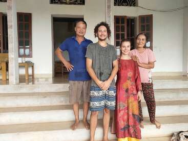 Cuatro personas sonríen en los escalones de una casa. Dos hombres, dos mujeres, de diferentes orígenes étnicos, vestidos de manera informal, parecen felices y relajados juntos.