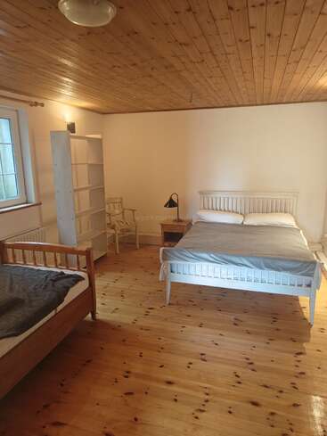 Dieses gemütliche Schlafzimmer verfügt über Holzböden und -decken, zwei Betten, ein Bücherregal, einen kleinen Tisch mit Lampe, einen Stuhl und ein Fenster für natürliches Licht.
