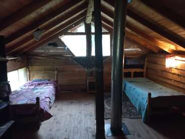 Esta acogedora habitación abuhardillada cuenta con paredes y techo de madera, dos camas individuales, una estufa de leña, ventanas pequeñas, mobiliario mínimo y una decoración sencilla y rústica con luz natural.