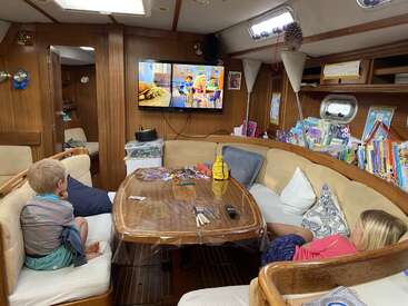 Dos niños se relajan en una acogedora cabaña de barco, viendo unos dibujos animados en la televisión. Hay libros, rompecabezas y manualidades repartidos por la mesa de madera y las estanterías.