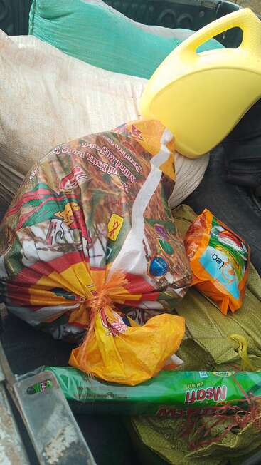 Une collection d'objets, dont un grand sac de riz, un jerrycan en plastique jaune, un tapis vert, un paquet de nourriture orange et une bobine de moustique dans le coffre d'un véhicule.
