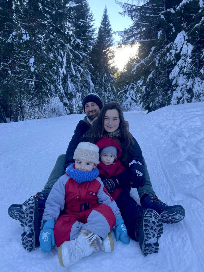 Das Bild zeigt eine dreiköpfige Familie, die im Schnee sitzt und von Bäumen umgeben ist. Der Vater und die Mutter umarmen ihr Kind und vermitteln so ein Gefühl von Wärme und Zusammengehörigkeit.