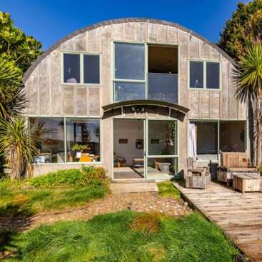 The image depicts a modern home with a unique design, featuring a flat roof and a large window, set against a backdrop of a serene outdoor space. The house is surrounded by a well-manicured lawn.