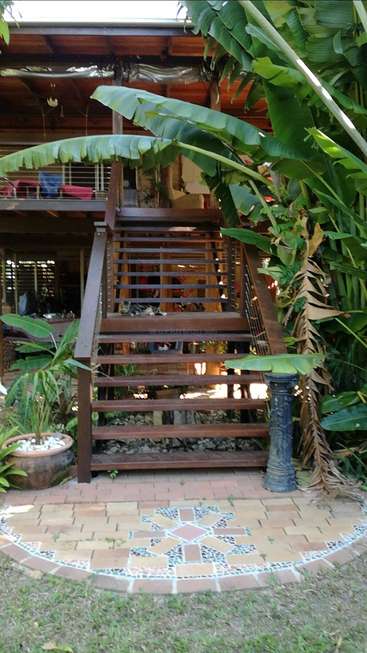 The image depicts a wooden staircase with a railing, surrounded by lush greenery and a decorative mosaic pattern on the ground.
