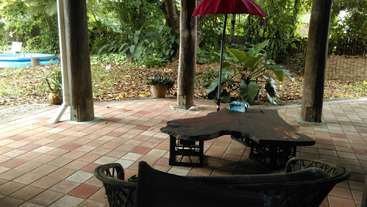 The image depicts a serene outdoor setting, featuring a patio area with a table and chairs, surrounded by lush greenery, evoking a sense of tranquility and relaxation.