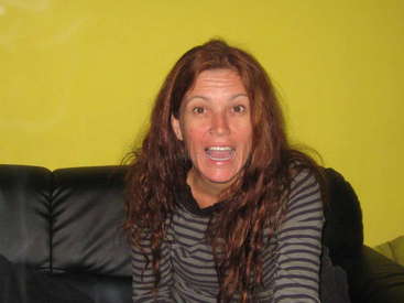 The image features a woman with long red hair, wearing a striped shirt, sitting on a black couch against a bright yellow wall, with a subtle watermark in the center.