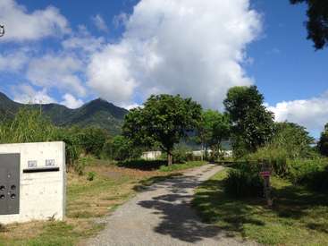 The image depicts a serene rural scene with a gravel road, lush trees, and a mailbox, set against a backdrop of majestic mountains under a blue sky with white clouds.