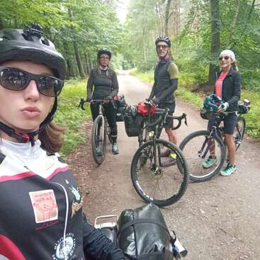 Quatro ciclistas posam em uma trilha na floresta, usando capacetes e óculos escuros. Suas bicicletas estão cheias de equipamentos, o que sugere uma aventura em grupo de bikepacking em meio a uma vegetação exuberante.