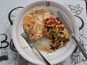 Sur une assiette blanche, deux œufs au plat saupoudrés de poivre côtoient un sauté coloré de chou, de carottes et de morceaux de bacon. Une fourchette et un couteau sont posés à côté.