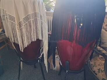 L'image montre deux tambours de conga rouges, chacun drapé d'un châle à franges, l'un blanc et l'autre noir, dans une pièce confortable et ensoleillée.