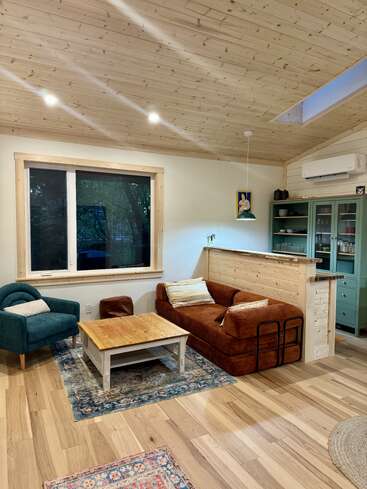 This cozy living room features wood floors and ceiling, a brown sofa, teal armchair, rustic coffee table, patterned rugs, green cabinet, and ambient lighting.
