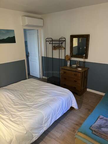 Dieses gemütliche Schlafzimmer verfügt über ein Doppelbett mit weißem Bettzeug, ein blaues Daybed, eine Holzkommode mit Spiegel, ein minimalistisches Hängeregal und eine geschmackvolle Einrichtung. Warme Atmosphäre.