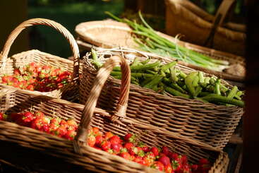 Three woven baskets filled with fresh produce sit in warm sunlight. Two baskets are full of ripe red strawberries, and one contains green beans.