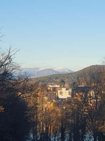 L'image représente une ville de montagne sereine, avec un groupe de bâtiments nichés parmi les arbres, dans le cadre majestueux de montagnes enneigées sous un ciel bleu clair.