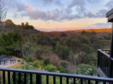 A imagem mostra uma paisagem serena com uma grade preta, árvores exuberantes e um céu vibrante com nuvens, tendo como pano de fundo uma colina.