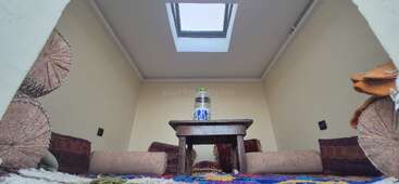 In diesem gemütlichen Raum steht ein niedriger Holztisch mit einer Wasserflasche, umgeben von Bodenkissen und Kopfkissen. Ein Oberlicht über dem Tisch lässt natürliches Licht herein und erhellt den Raum.