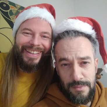 L'image montre deux hommes portant des bonnets de Père Noël, posant pour un selfie, la tête de l'un reposant sur l'épaule de l'autre, les deux ayant des expressions neutres.