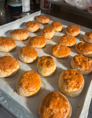 Unas galletas doradas descansan sobre una bandeja de horno forrada con papel vegetal, recién horneadas y resplandecientes bajo la cálida luz del sol, listas para ser degustadas en el acogedor ambiente de una cocina.