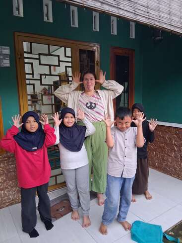 Fünf Kinder und ein Erwachsener posieren spielerisch vor einem Haus, machen lustige Grimassen und Handgesten, wirken fröhlich und genießen ihre gemeinsame Zeit.