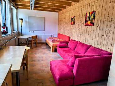 Cette chambre confortable est composée d'un canapé rose vif, d'un lit simple, de murs en bois, de deux bureaux, d'une lampe, d'œuvres d'art murales colorées et de grandes fenêtres pour la lumière naturelle.